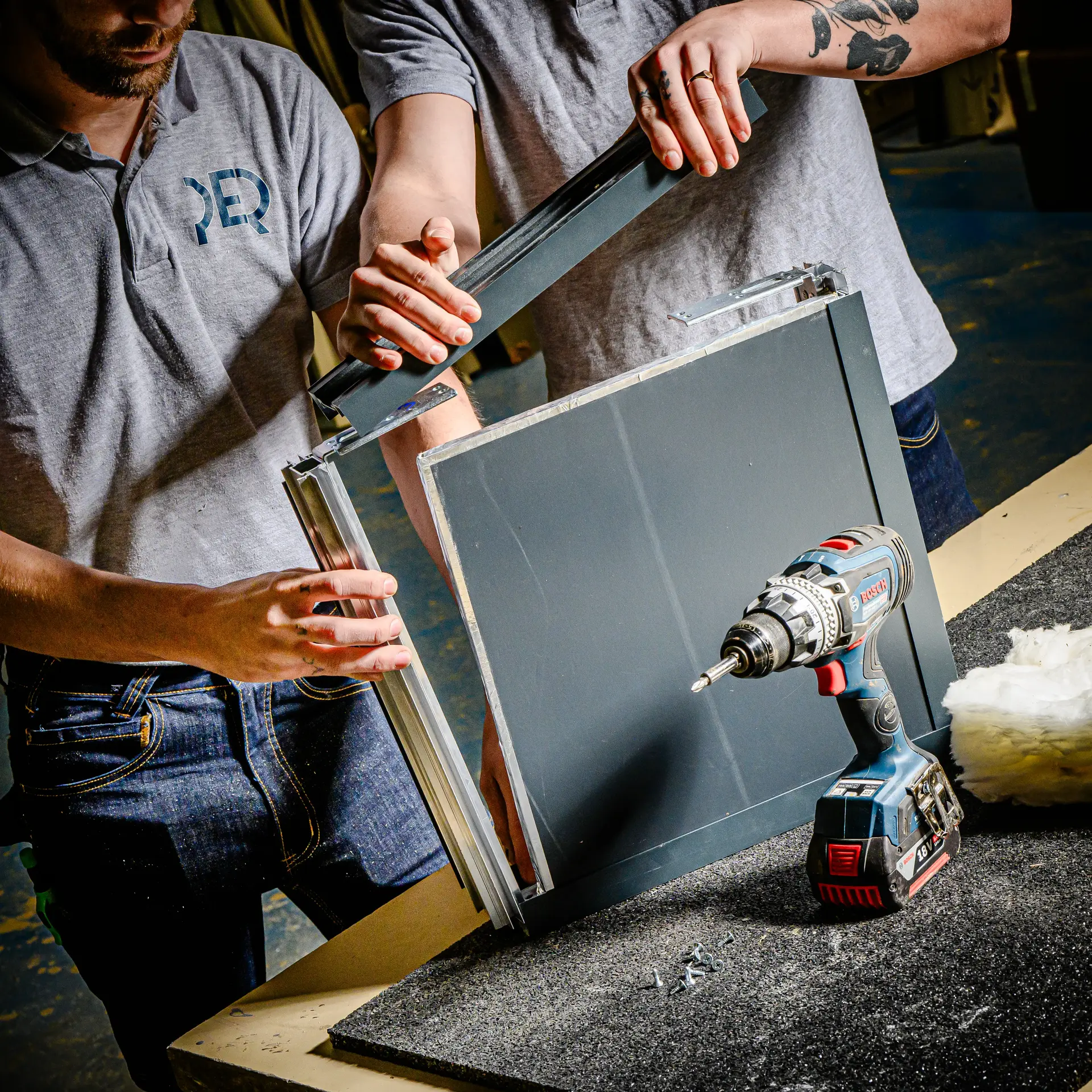 Polo de travail 'PER' brodé porté par un artisan lors de travaux d'assemblage en atelier.